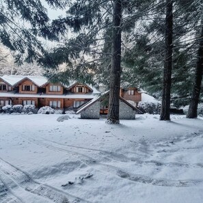 A wooden cabin with a stone foundation, surrounded by snow-covered trees.