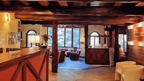 Interior rústico com piso de pedra, vigas de madeira, espaço de bar e assentos.