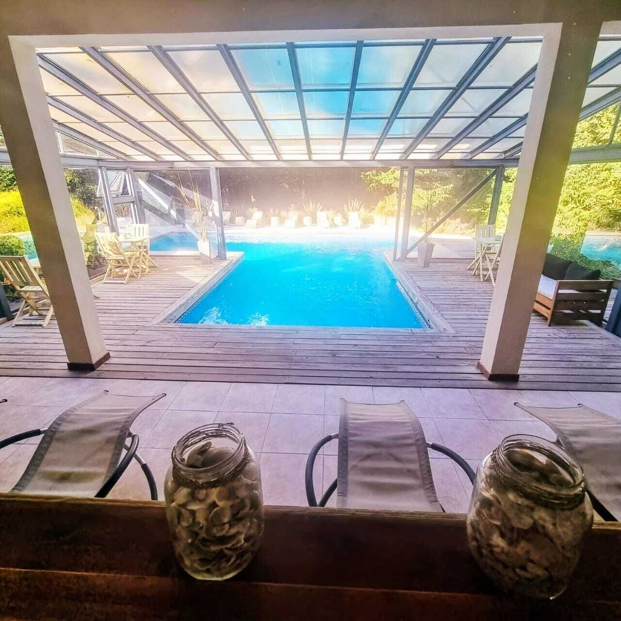 Ein Poolbereich mit Glasdach, Liegestühlen und einer Holzterrasse.