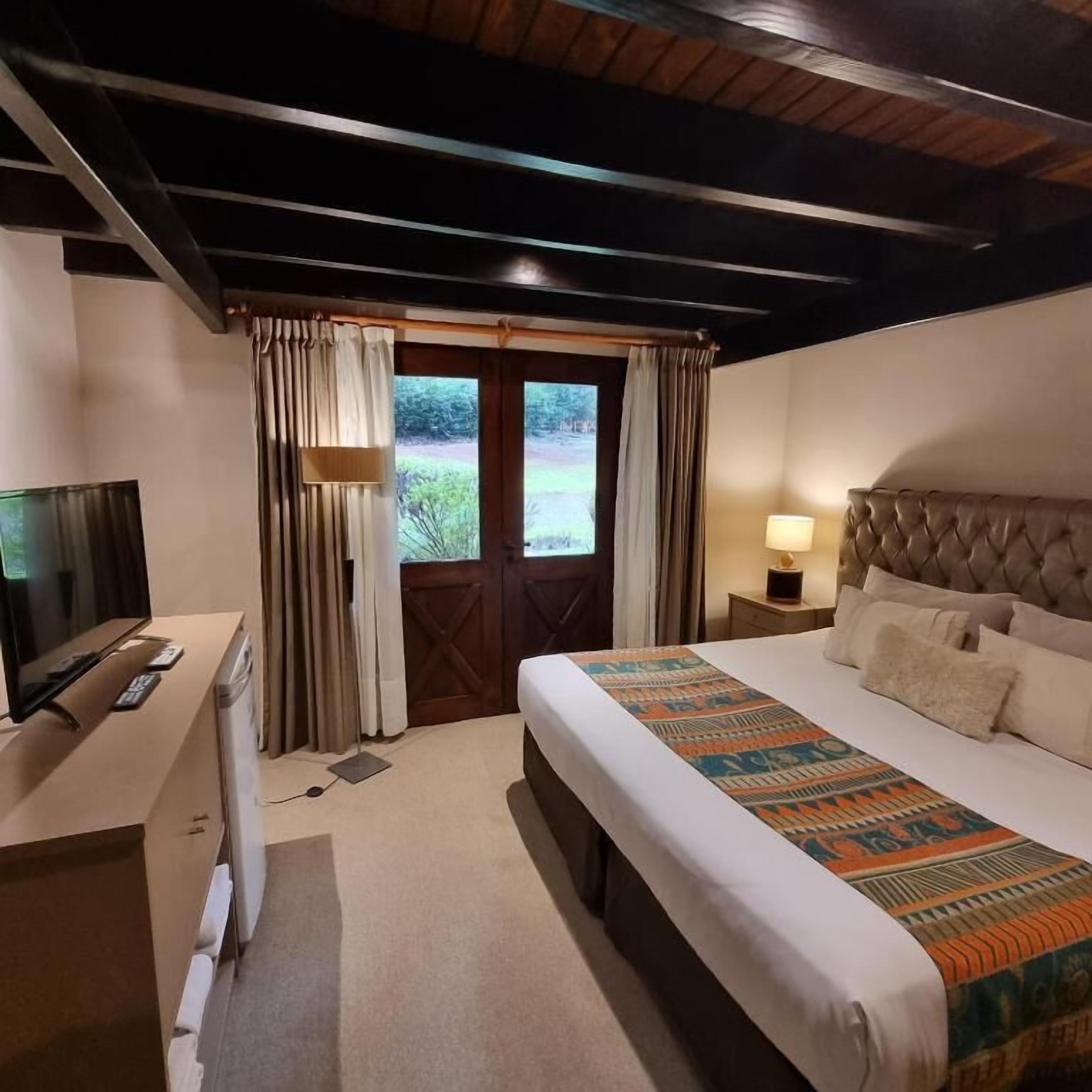 A hotel room with a bed, a desk, a television, and a window with curtains.