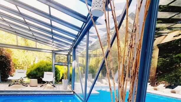 Piscina interna com cobertura de vidro, deck de madeira e espreguiçadeiras.