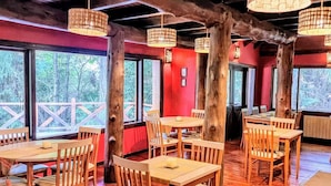 Um restaurante com mesas e cadeiras de madeira, grandes janelas e luminárias pendentes.