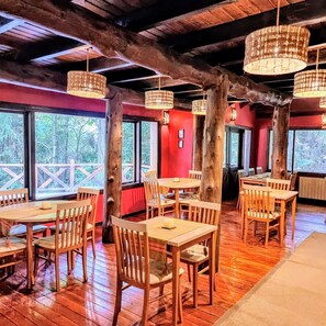 A restaurant with wooden tables and chairs, large windows, and hanging lamps. - Hosteria Altos Los Pioneros  (Villa La Angostura)