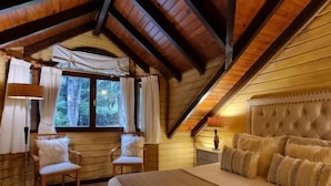 Quarto com cama grande, duas cadeiras, janela com cortinas e teto de madeira.