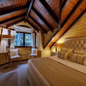 A bedroom with a large bed, two chairs, a window with curtains, and a wooden ceiling. - Hosteria Altos Los Pioneros  (Villa La Angostura)