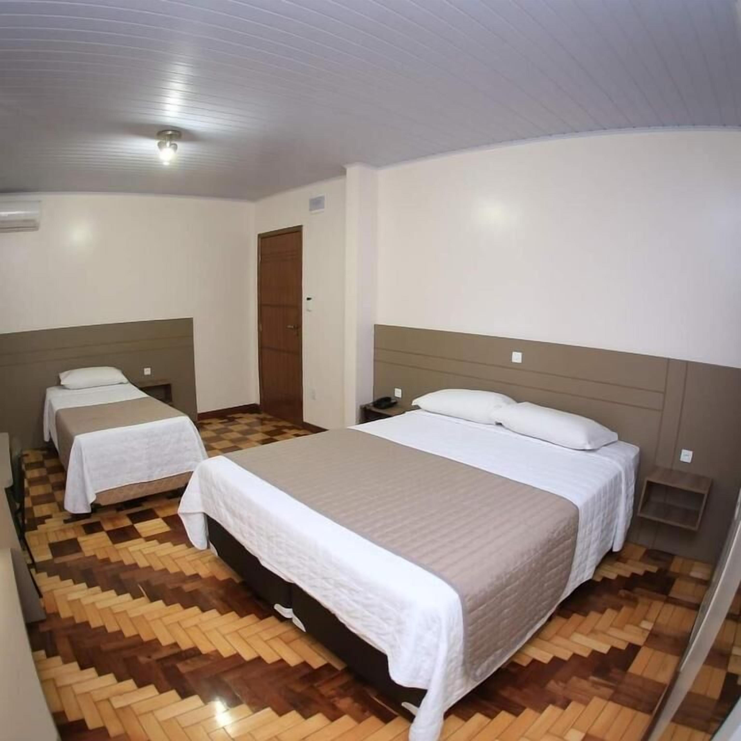 A hotel room with a large bed, two smaller beds, a wooden parquet floor, and a plain white ceiling.