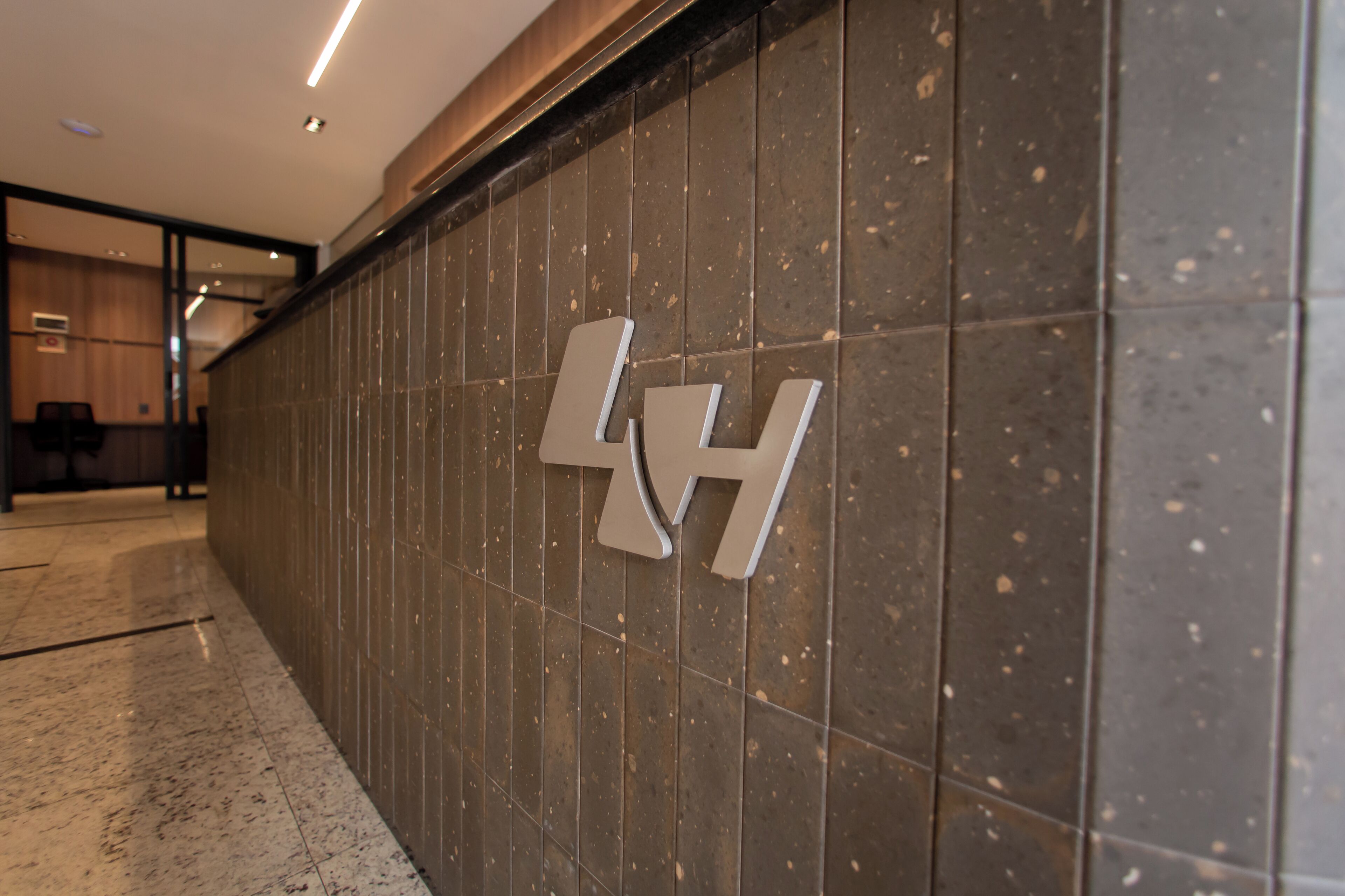 A hallway with a dark tiled wall featuring a large, metallic letter 'H' logo.