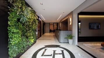 A hotel reception area with a reception desk, a large logo on the floor, a wall with greenery, and a television screen.