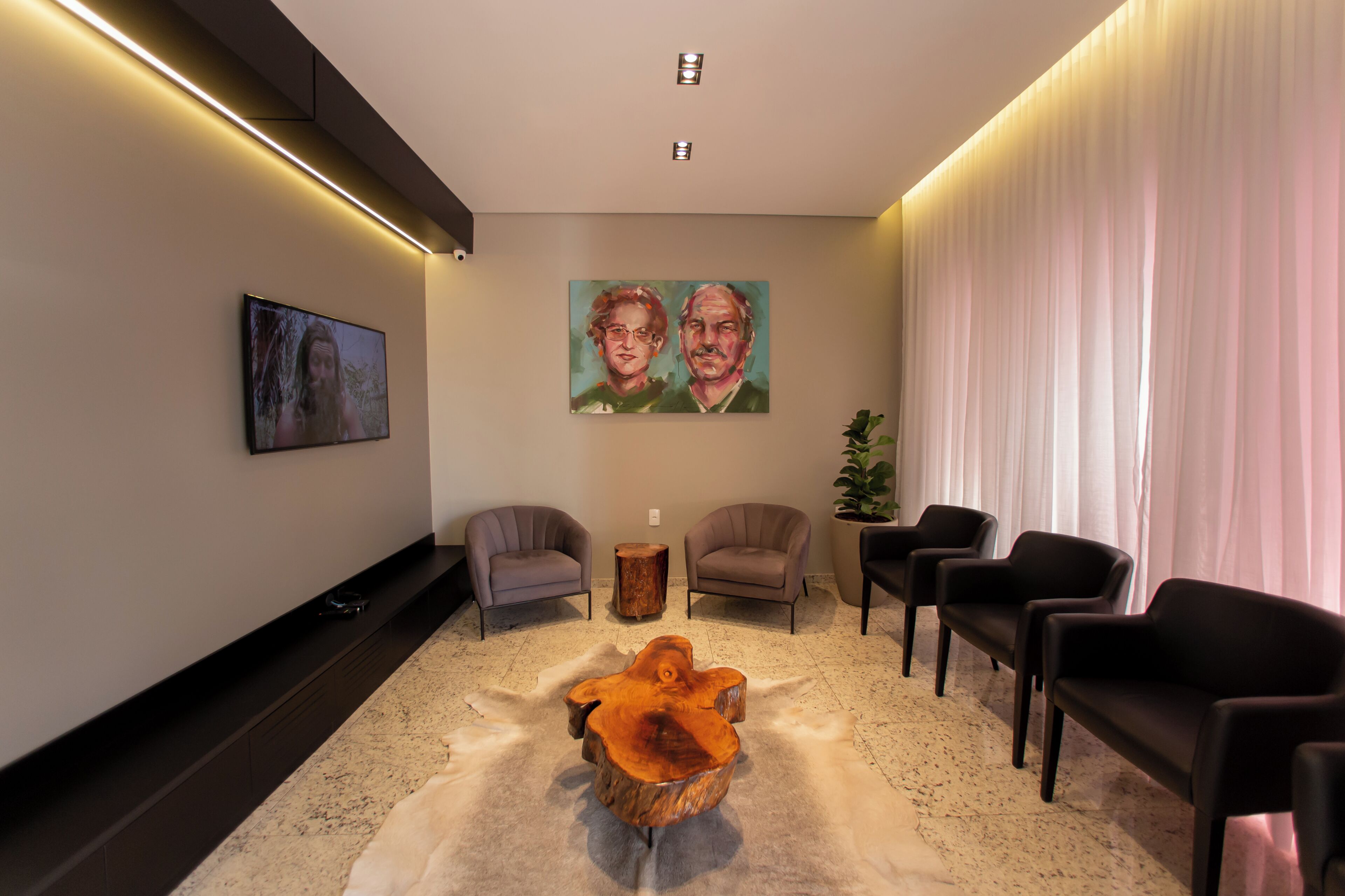 A modern lobby with a flat-screen TV, two paintings, a wooden coffee table, and several chairs.