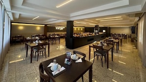 Un amplio comedor de hotel con varias mesas y sillas, una estación de buffet y un diseño moderno de techo.