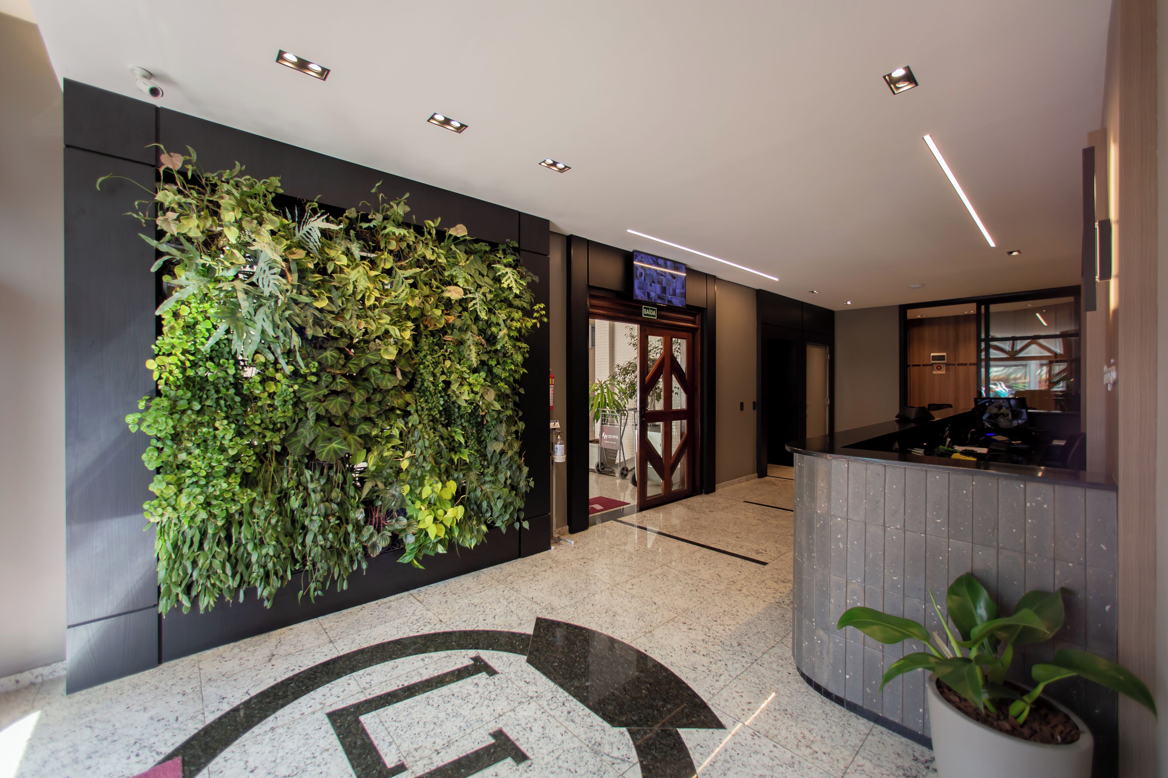 A lobby with a reception desk, a wall with a vertical garden, and a door marked 'SAIDA'.