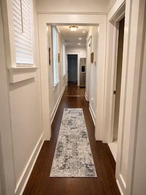 A hallway with a patterned rug, white walls, and a door at the end.
