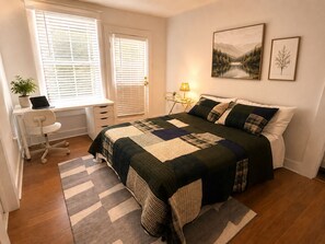 Une chambre à coucher avec un lit, un bureau, une chaise, une lampe et deux tableaux encadrés accrochés au mur.
