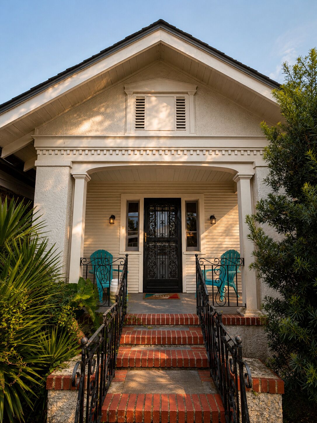 A two-story house with a front porch, a black door, and two blue Adirondack chairs.