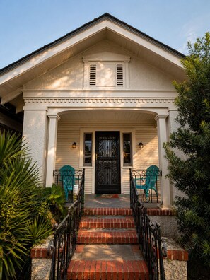 A two-story house with a front porch, a black door, and two blue Adirondack chairs.