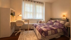 A bedroom with a bed, desk, chair, and a window with curtains.