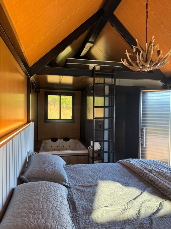 A bedroom with a bed, a window, a desk, and a chandelier.