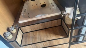 Un suelo de madera con un estante de metal negro, un armario de madera y una bañera blanca con cabezal de ducha.