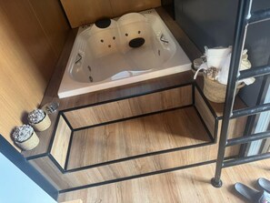 Een houten vloer met een zwart metalen rek, een houten kast en een witte badkuip met douchekop.