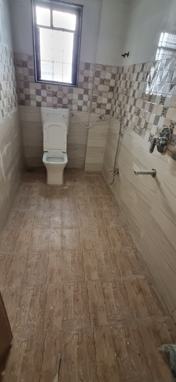 A bathroom with a toilet, a shower, and a window.