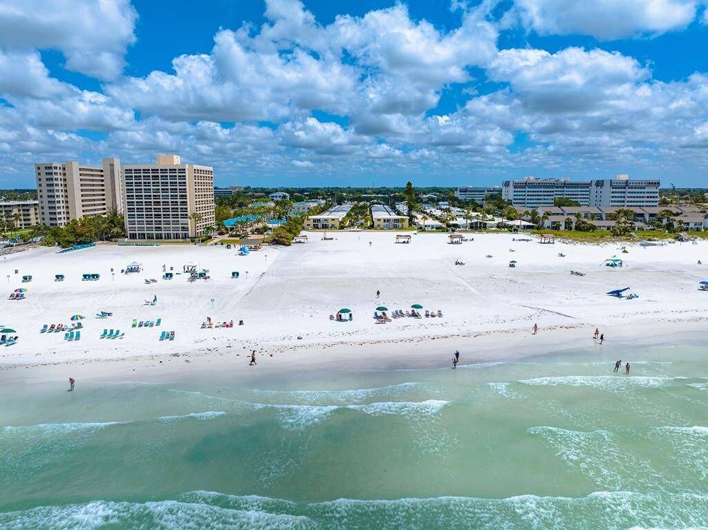 A beach with clear waters, a sandy shore, and buildings in the background.