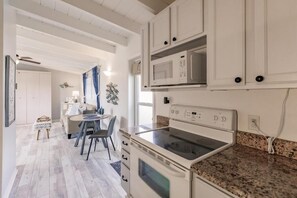 Una cocina compacta con armarios blancos, microondas, horno y encimera de granito.
