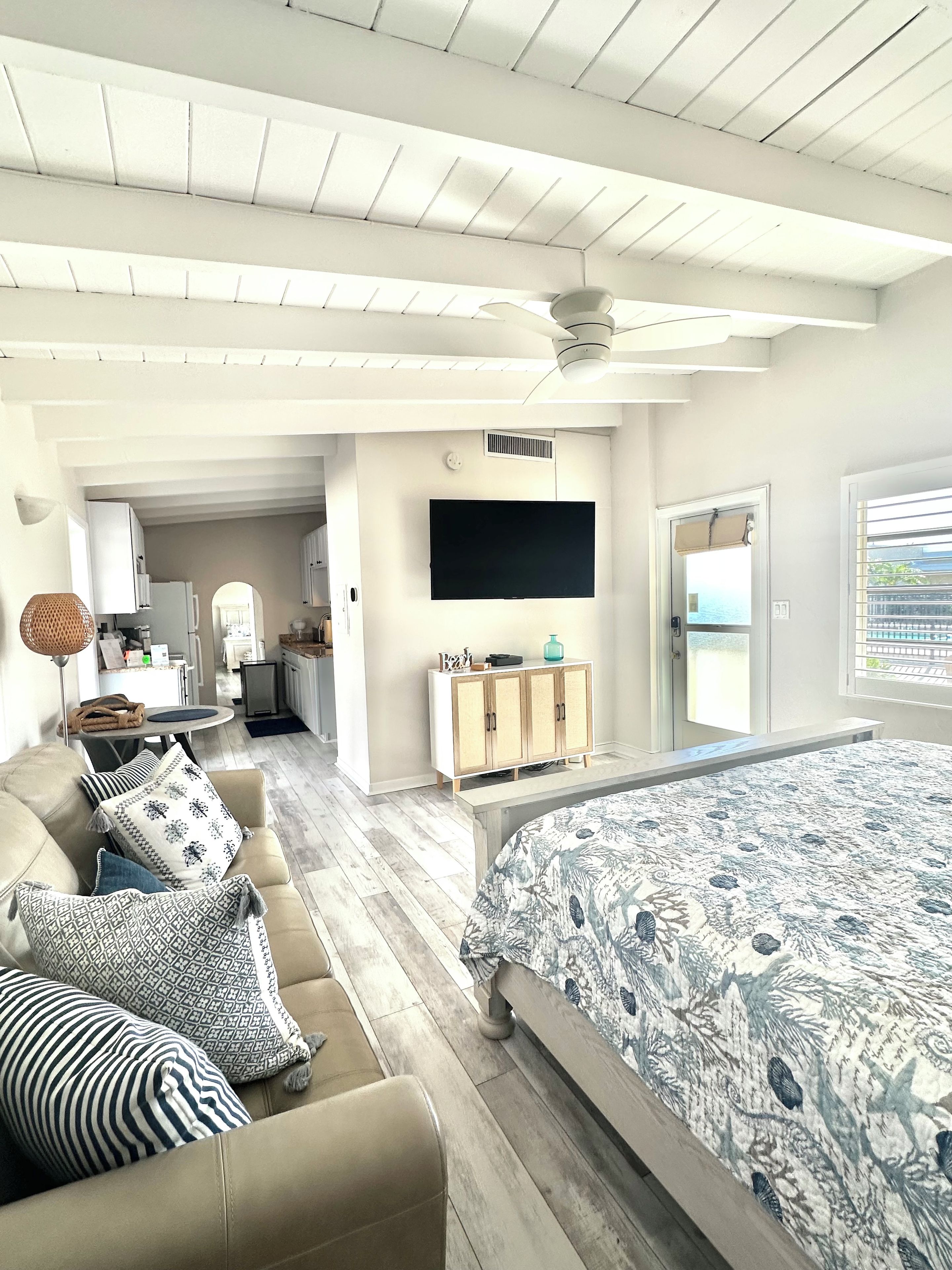 A modern bedroom with a large bed, a sofa, a TV, and a view of the sea.