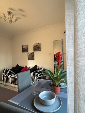 A dining area with a table set for two, a potted plant, and a wine glass. - Central London 25 min - Cosy Tooting 2 bed house by tube station (London)