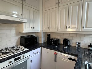 A kitchen with white cabinets, a black countertop, a stove, a toaster, and a dishwasher. - Central London 25 min - Cosy Tooting 2 bed house by tube station (London)
