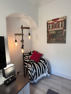 A modern room with a zebra-patterned bed, a red pillow, a vintage-style wall art of a market, and a desk with a lamp. - Central London 25 min - Cosy Tooting 2 bed house by tube station (London)