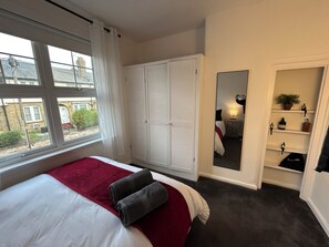 A bedroom with a bed, a wardrobe, a mirror, and a shelf with toiletries. - Central London 25 min - Cosy Tooting 2 bed house by tube station (London)