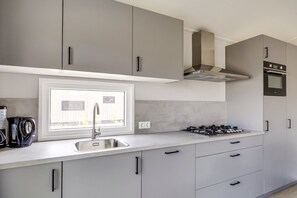 Une cuisine moderne avec des meubles gris, un évier en acier inoxydable, une cuisinière à gaz et une fenêtre au-dessus de l’évier.