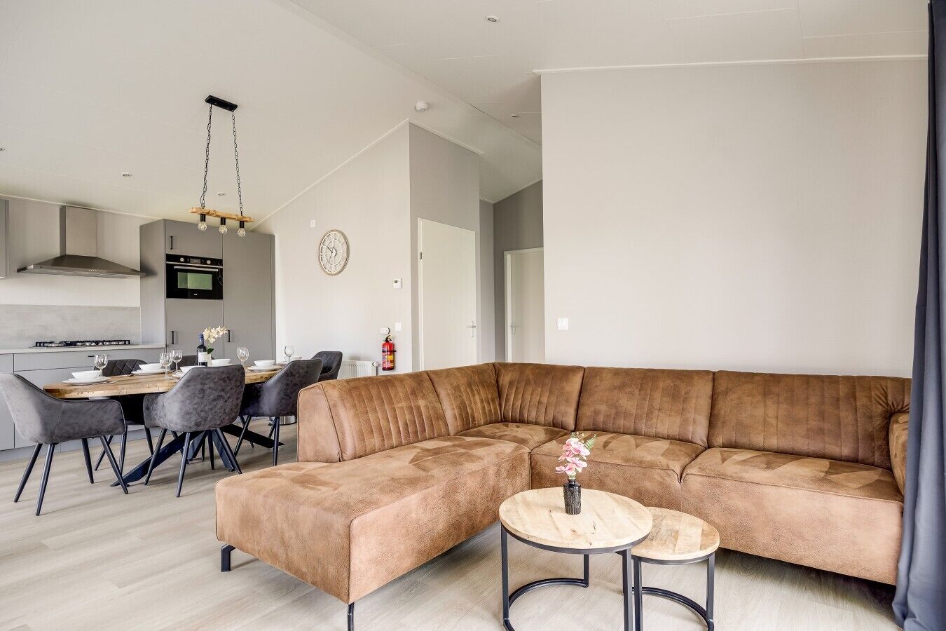 Una sala de estar moderna con un sofá modular, un comedor con mesa de madera y una cocina al fondo.