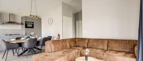 Ein modernes Wohnzimmer mit einer Eckcouch, einem Essbereich mit Holztisch und einer Küche im Hintergrund.