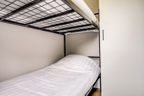 A single bed with a metal frame and a white mattress in a room with a slanted ceiling and a white wall. - Villa Riant 64 | Ruim vakantiehuis met airco | Zennewijnen, Betuwe (Zennewijnen)