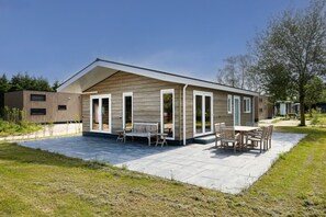 Une maison moderne de plain-pied dotée d’une terrasse, d’un coin repas et d’un petit jardin.
