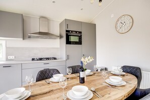A modern kitchen with grey cabinets, a built-in oven, and a dining area with a wooden table set for two. - Villa Riant 64 | Ruim vakantiehuis met airco | Zennewijnen, Betuwe (Zennewijnen)