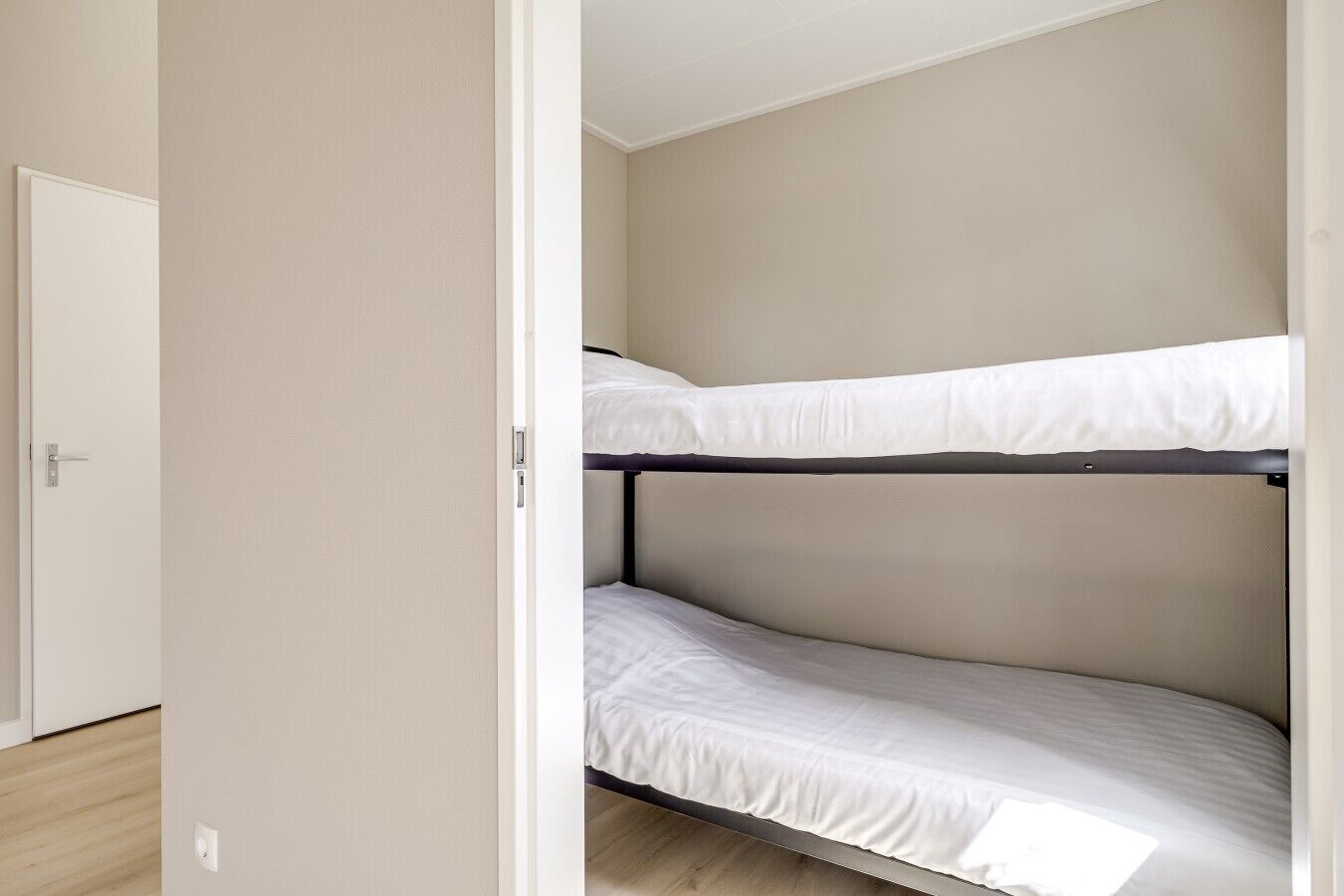A bunk bed in a room with a door and a light switch on the wall.