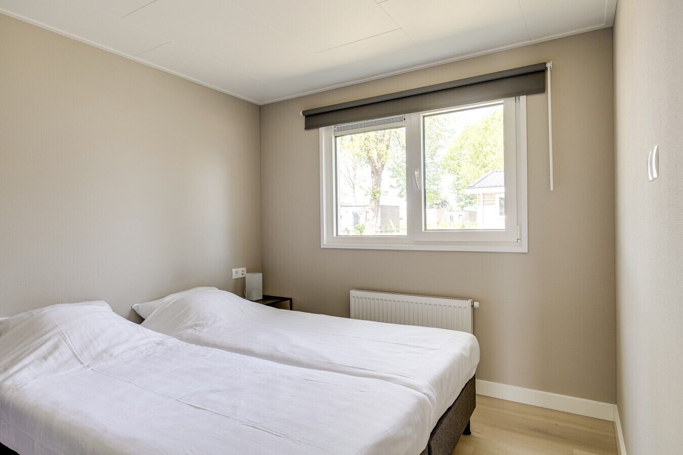 Et soveværelse med to senge, et vindue med udsigt til træer og en radiator.
