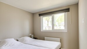 Et soveværelse med to senge, et vindue med udsigt til træer og en radiator.
