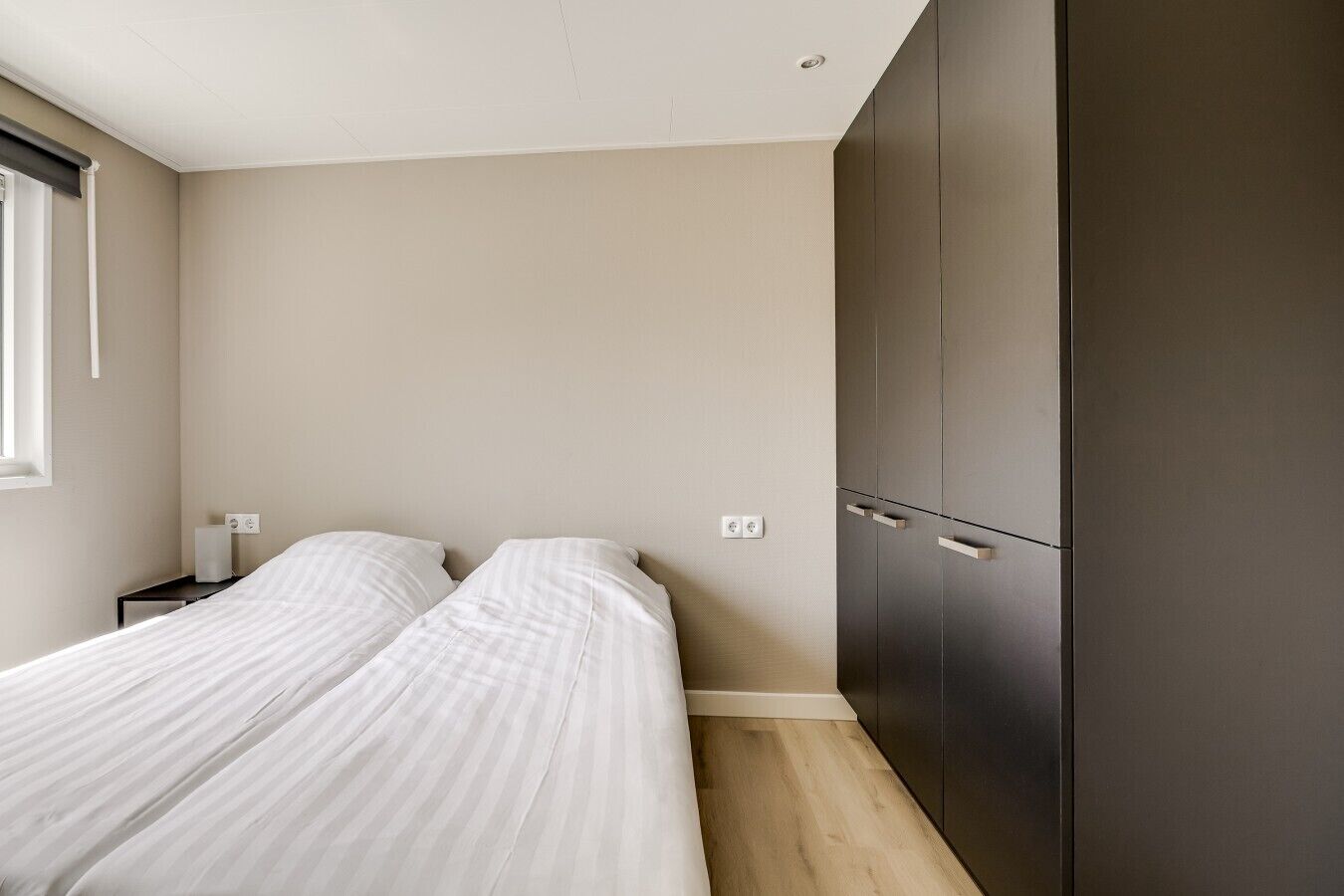 Une chambre avec deux lits, une armoire, une table de chevet et une fenêtre.