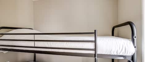 A bunk bed with a metal frame and white bedding in a room with plain walls and a window.