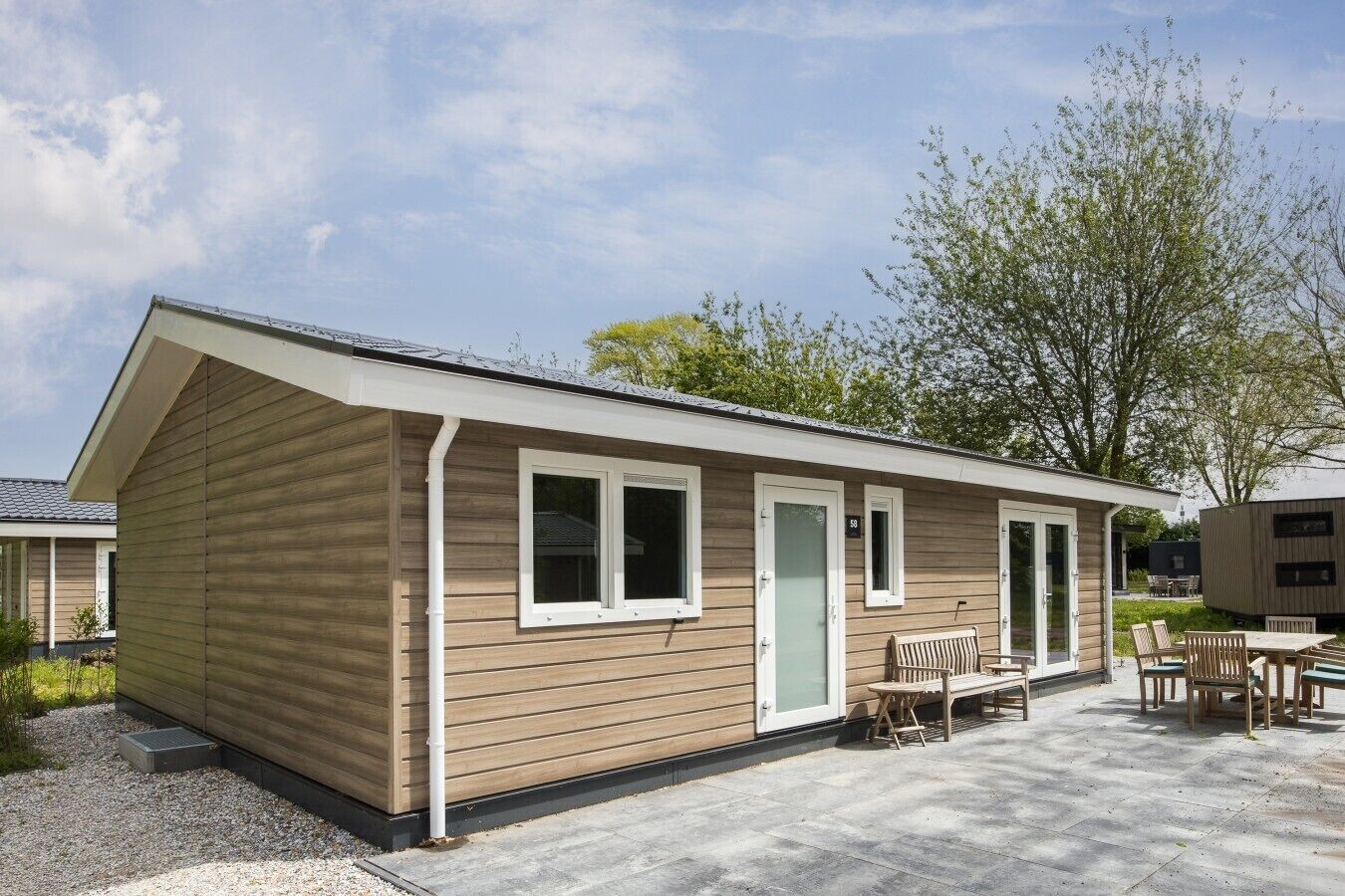 A single-story building with a sloped roof, a front door, and a small patio area with outdoor furniture.