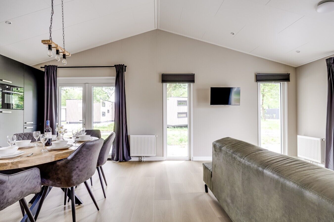 A modern living room with a sofa, a dining table set for four, and a television mounted on the wall.