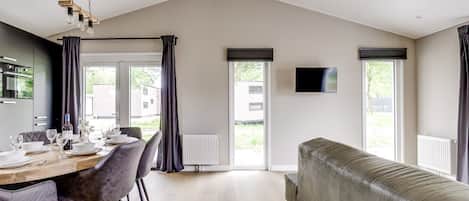 Ein modernes Wohnzimmer mit einer Couch, einem Esstisch für vier Personen und einem an der Wand befestigten Fernseher.