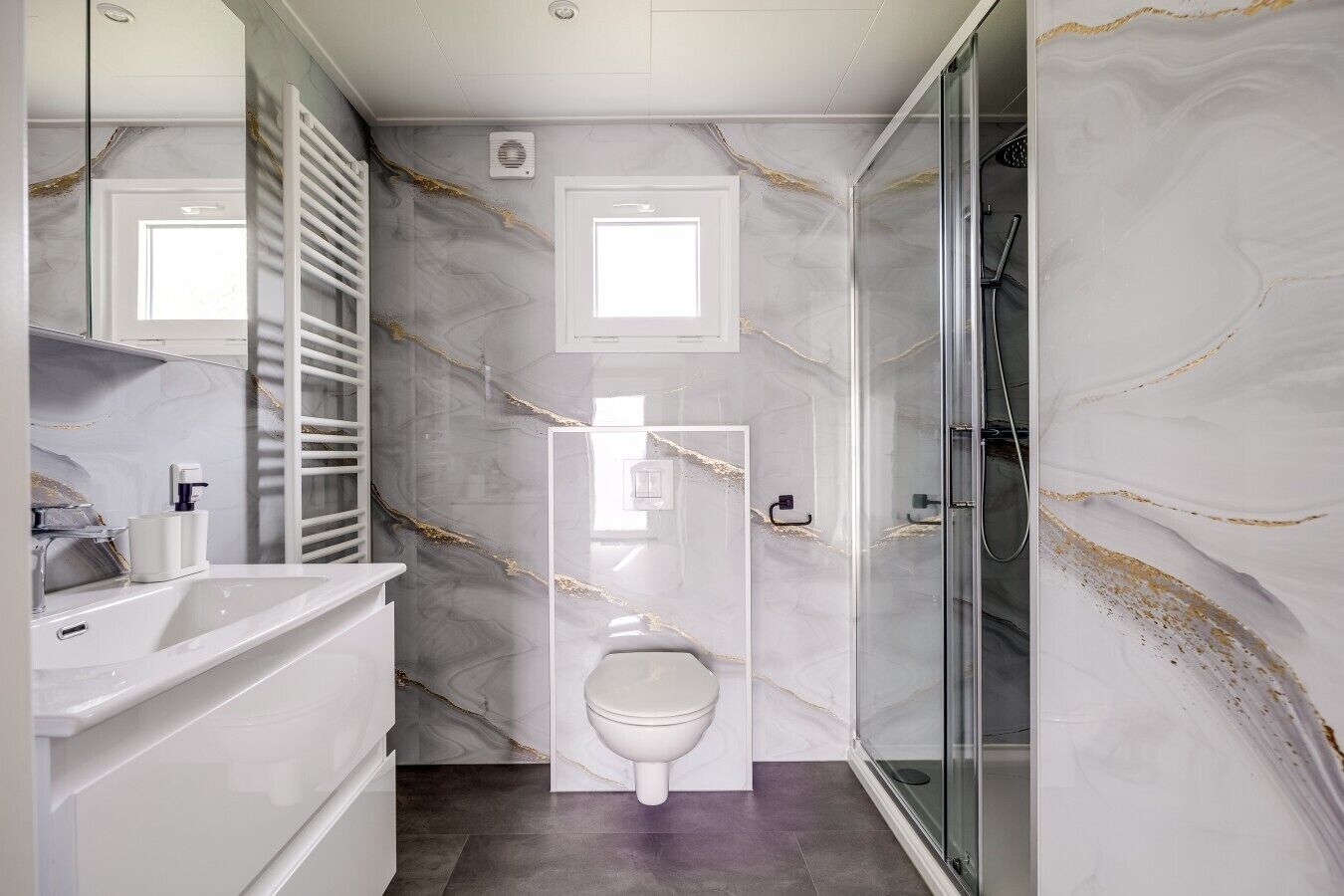 A bathroom with a marble wall, a white sink, a toilet, and a glass shower enclosure.