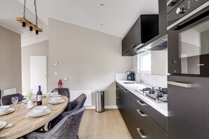 A modern kitchen with a dining area, featuring stainless steel appliances, a wooden dining table, and a pendant light fixture. - Villa Riant 58 | 6 persoons vakantiehuis (Zennewijnen)