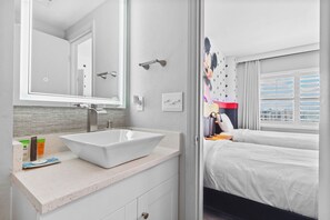 Un bagno moderno con un ampio lavandino bianco, uno specchio e uno spazio doccia.
