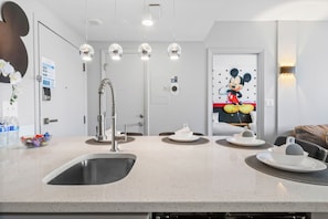 A modern kitchen with a sink, a coffee maker, and a Mickey Mouse mural on the wall. - 2BR apartment with king bed near universal (Orlando)