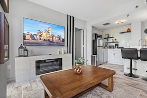 A modern living room with a flat-screen TV, a fireplace, and a dining area. - 2BR apartment with king bed near universal (Orlando)